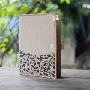 Beige juco file folder partly open, with a dark leaf-and-stem motif across the lower front, beige binding and a short tab.