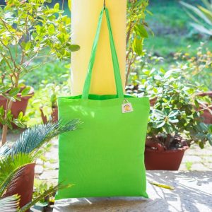 Lime-green cotton tote bag with long shoulder straps hanging from a hook outdoors