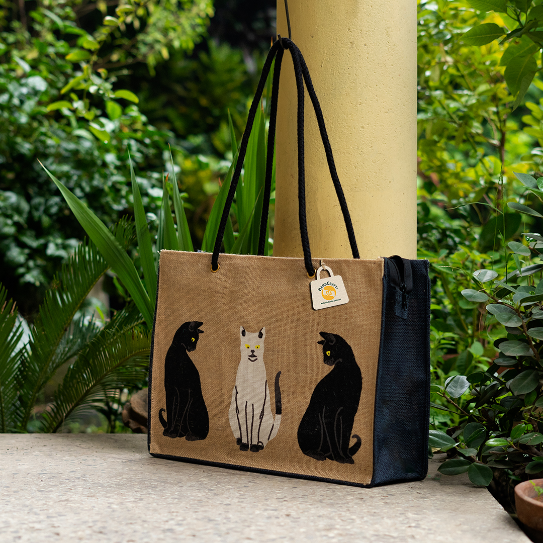 Bag with three cat motifs, dark sides and long dark handles.